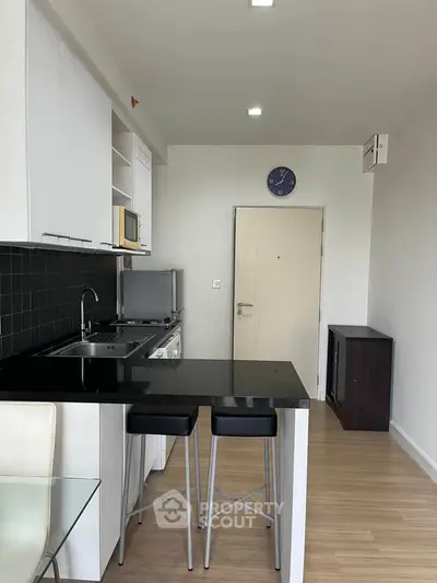 Modern kitchen with sleek black countertops and bar stools in a stylish apartment.