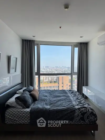 Modern bedroom with large window offering stunning city view, featuring stylish decor and ample natural light.