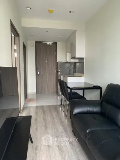 Modern apartment interior with sleek black leather sofa and compact kitchen area.