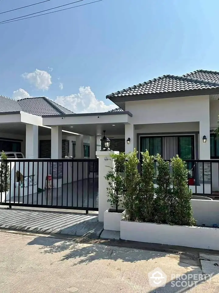 Modern single-story house with gated entrance and manicured shrubs under clear blue sky.