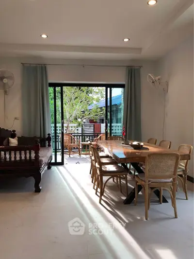 Spacious living room with elegant dining area and large windows opening to a balcony with garden view.