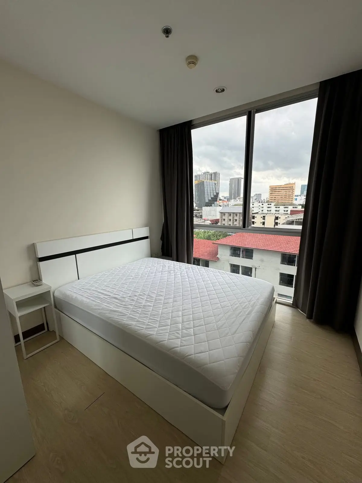 Modern bedroom with large window offering city views, featuring a minimalist design and ample natural light.