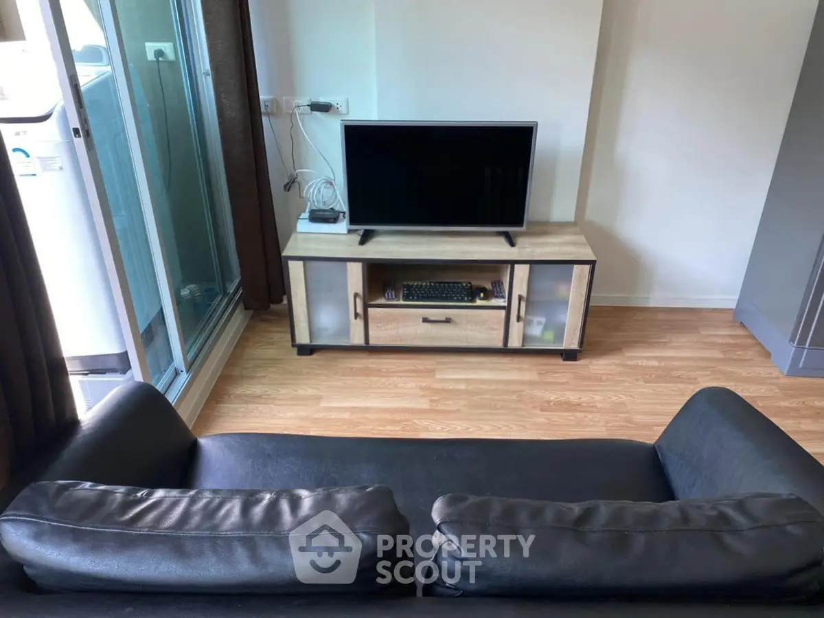 Modern living room with sleek black sofa and flat-screen TV on wooden stand, featuring glass sliding doors.