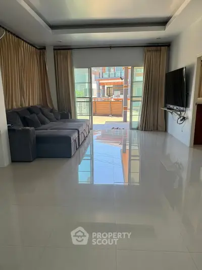 Spacious living room with modern sofa and wall-mounted TV, featuring large windows and glossy tiled floors.
