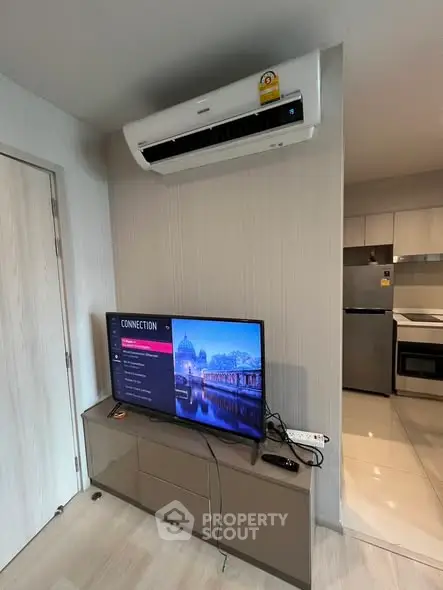 Modern living room with air conditioning and sleek TV setup, adjacent to a contemporary kitchen.