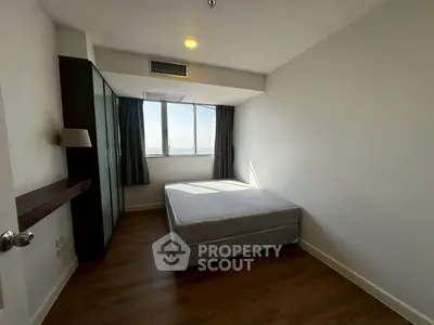 Spacious bedroom with large window and wooden flooring in modern apartment