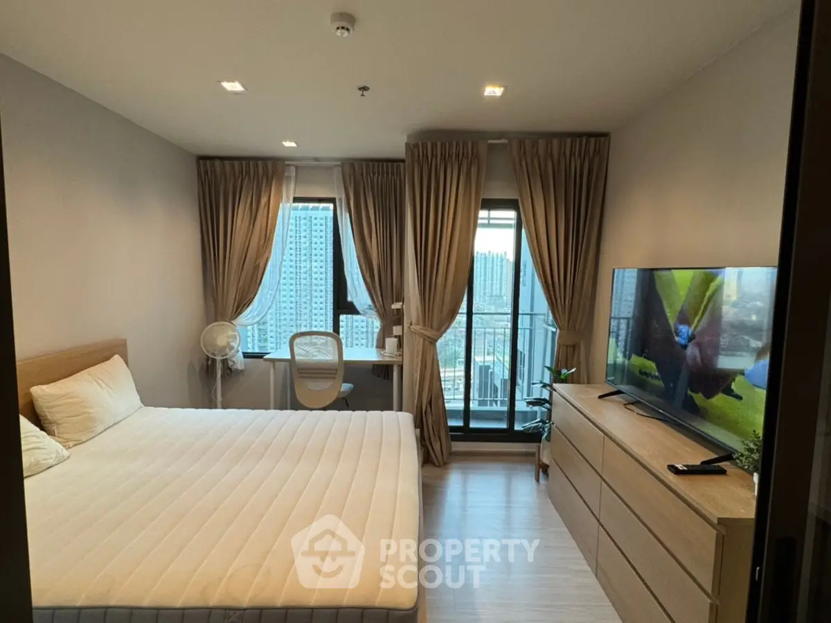 Modern bedroom with city view, featuring a cozy bed, large TV, and elegant curtains.