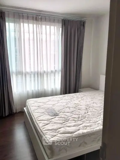Cozy bedroom with large window and elegant curtains, featuring a comfortable mattress.