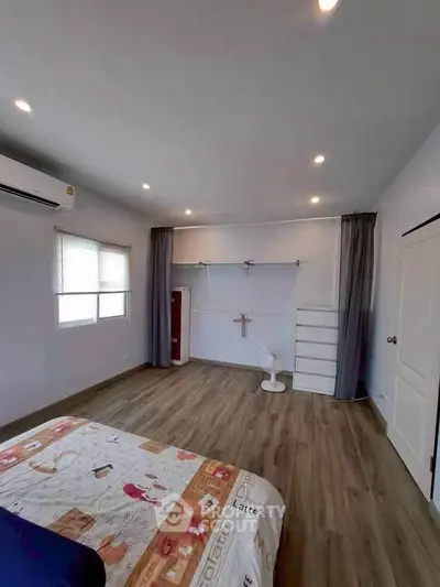 Spacious bedroom with modern decor and wooden flooring, featuring ample natural light and stylish furnishings.