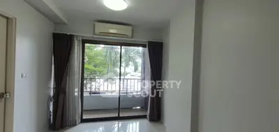 Spacious room with balcony and large windows offering natural light and greenery view.