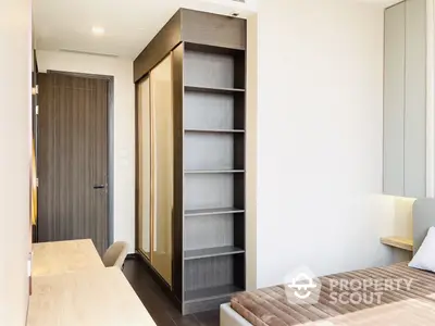 Modern bedroom with built-in wardrobe and shelving unit, featuring a minimalist design and ample natural light, ideal for urban living.