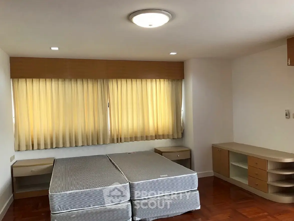 Spacious bedroom with twin beds and wooden furniture, featuring large window with curtains.