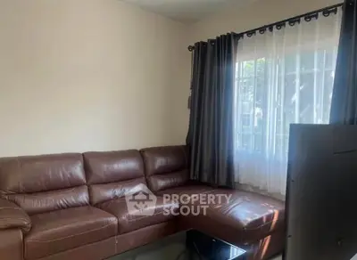 Cozy living room with brown leather sectional sofa and large window with curtains.