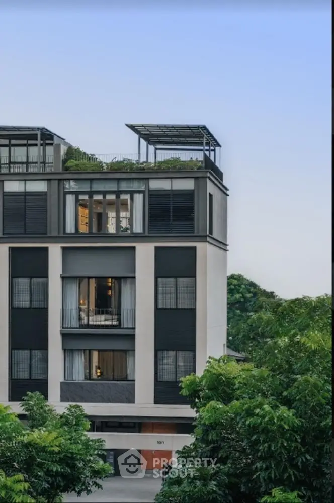 Modern multi-story building with rooftop garden and large windows in lush green setting.