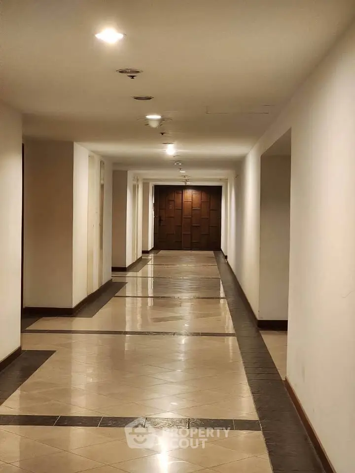 Elegant corridor with polished tiles leading to a wooden door in a modern building.