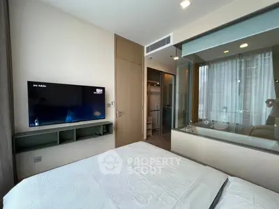 Modern bedroom with TV and glass wall overlooking bathroom in luxury apartment.