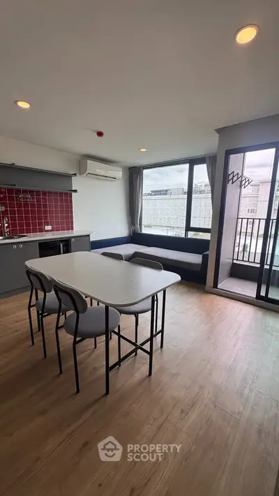 Modern open-layout living room with dining area and balcony access, featuring stylish furniture and city views.