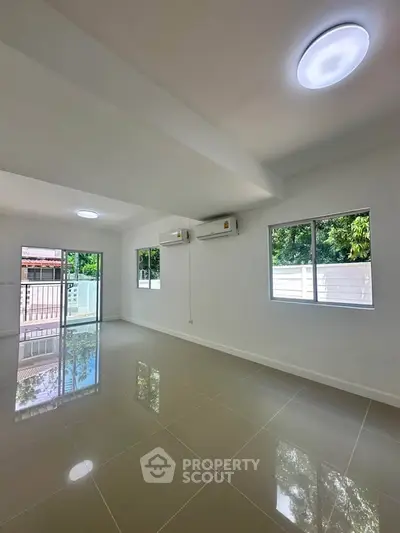 Spacious living room with large windows and glossy tiled floors, offering a bright and airy atmosphere.