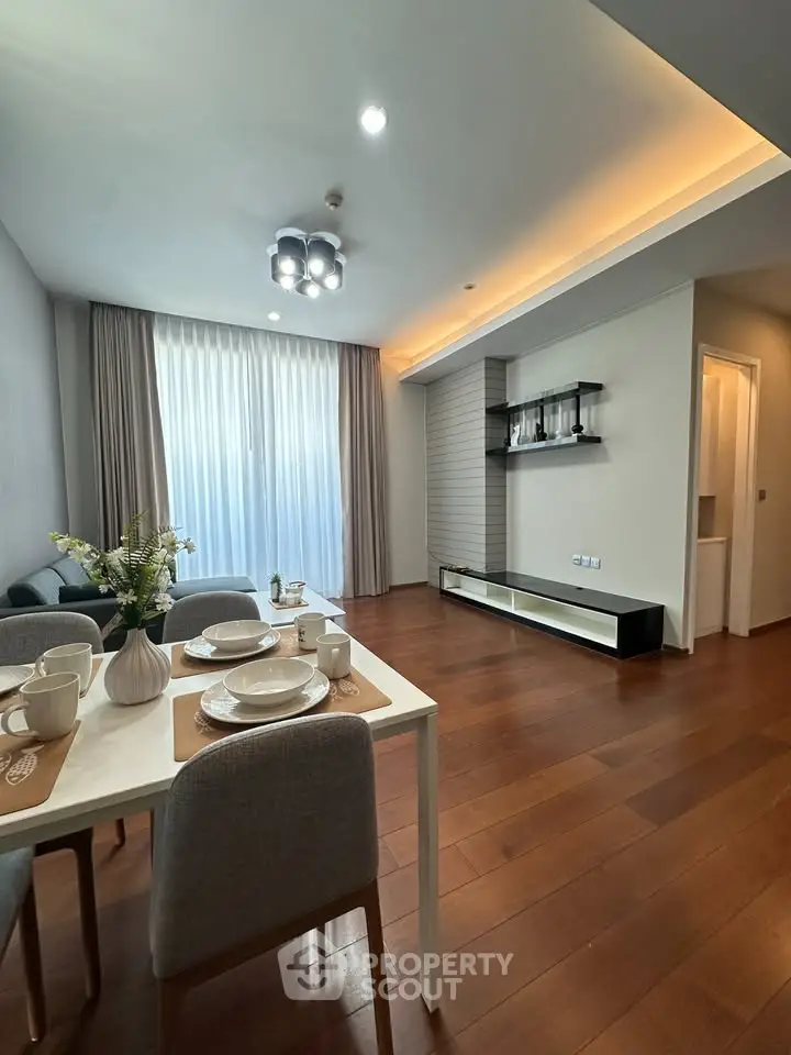 Modern living room with dining area, wooden flooring, and elegant lighting in a stylish apartment.