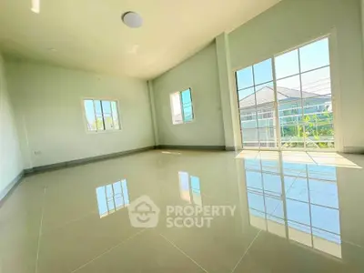 Spacious sunlit room with glossy tiled floors and large windows in modern home.