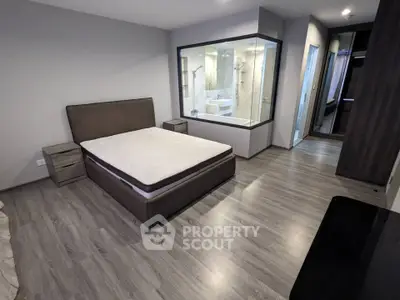 Modern bedroom with glass-walled bathroom, sleek flooring, and stylish furnishings.