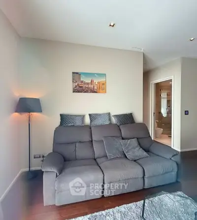 Modern living room with cozy gray sofa and stylish decor, adjacent to a sleek bathroom.