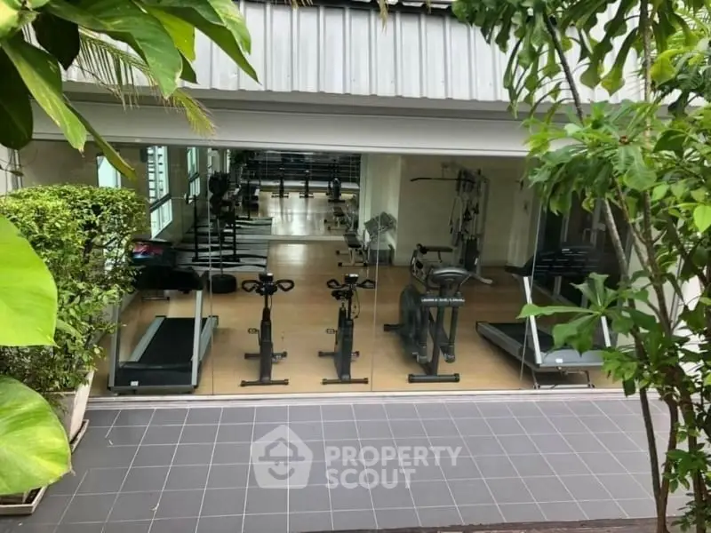 Modern gym with exercise equipment and large glass windows in a residential building.
