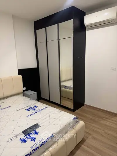 Modern bedroom with sleek wardrobe and air conditioning unit, featuring a comfortable bed and wooden flooring.