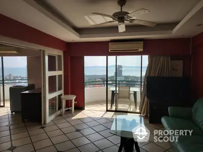 Spacious living room with terracotta tiles, ceiling fan, and large windows offering an expansive city view, leading to a sunny balcony.