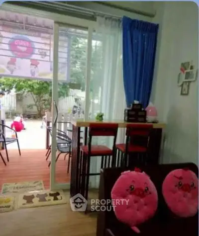 Charming living room with sliding glass doors opening to a cozy outdoor patio, featuring playful decor and vibrant seating.