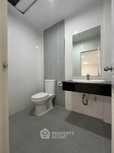 Modern bathroom with sleek design, featuring a toilet and a wall-mounted sink with a large mirror.