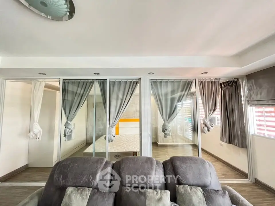 Spacious living room with modern decor and glass partitions leading to a cozy bedroom.