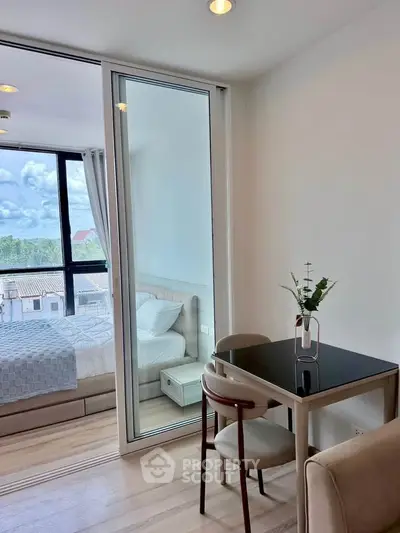 Modern apartment with glass partitioned bedroom and cozy dining area, featuring elegant decor and natural light.