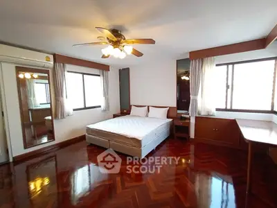 Spacious bedroom with polished wooden floors and ceiling fan in modern apartment.