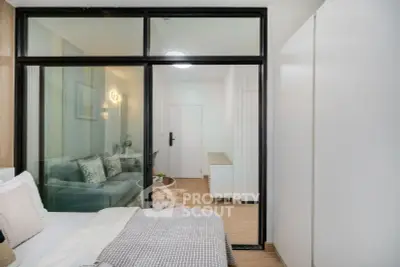 Modern bedroom with glass partition leading to cozy living area, featuring stylish decor and neutral tones.