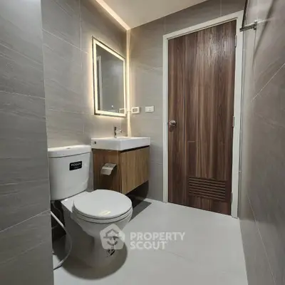 Modern bathroom with sleek design, featuring a toilet, illuminated mirror, and wooden vanity.