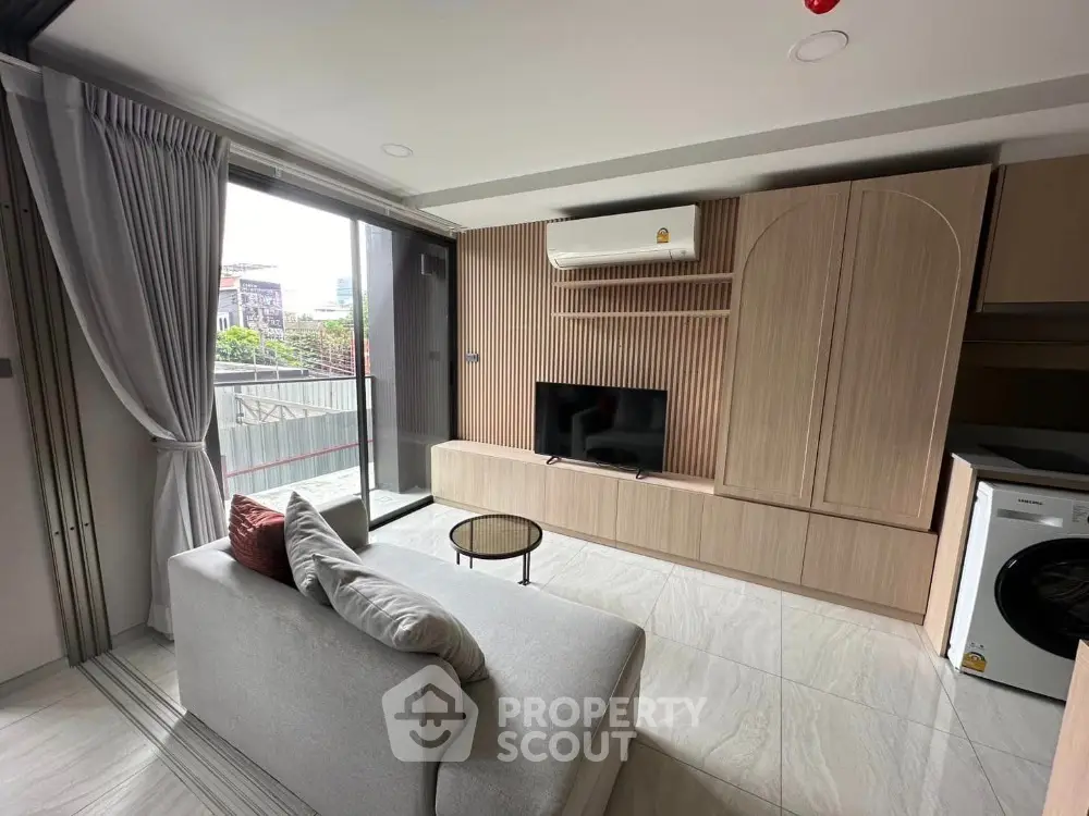 Modern living room with balcony, sleek furniture, and built-in appliances in a stylish apartment.