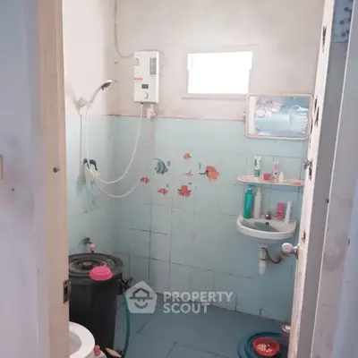 Compact bathroom with shower and wall-mounted water heater, featuring light blue tiles and small window.