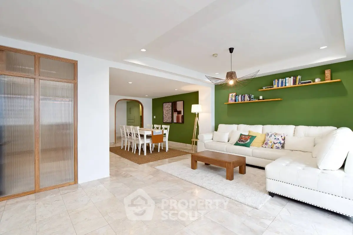 Spacious living room with elegant decor and dining area, featuring a cozy white sofa and stylish green accent wall.