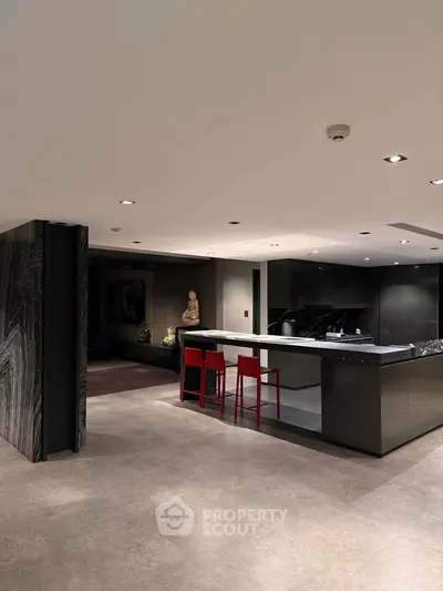 Luxurious modern kitchen with sleek black cabinetry and red bar stools in a spacious open layout.