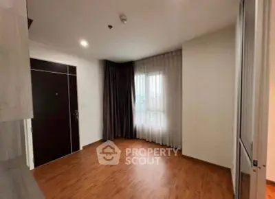 Spacious empty room with wooden flooring and large window, ideal for customization.