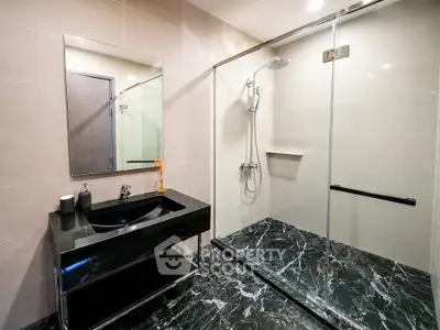 Luxurious modern bathroom with sleek black marble flooring and spacious glass shower enclosure.