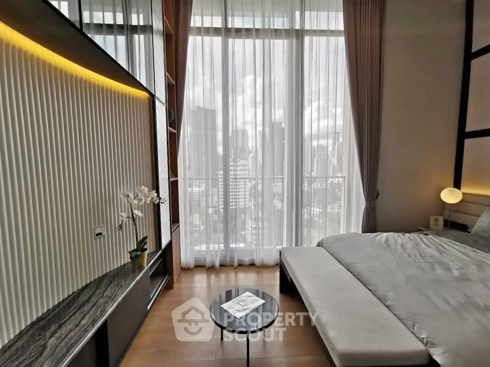 Luxurious bedroom with floor-to-ceiling windows offering stunning city views, modern decor, and elegant furnishings.