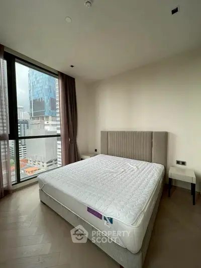 Modern bedroom with large window and city view, featuring a stylish bed and neutral decor.