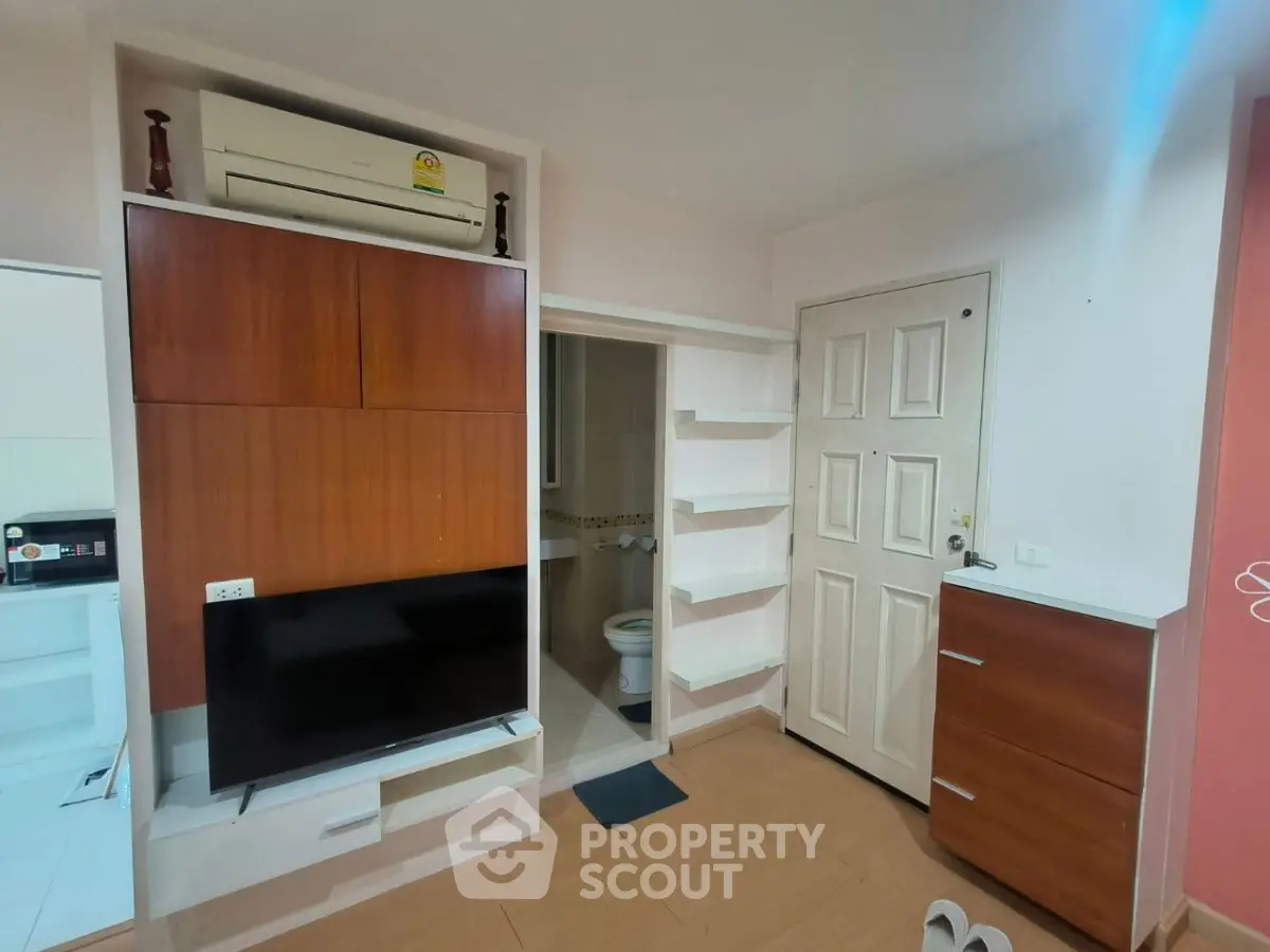 Compact living space with wall-mounted TV and air conditioning, featuring a small bathroom entrance.