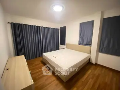 Spacious bedroom with wooden flooring and modern curtains