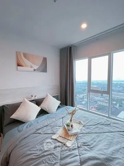 Modern bedroom with large windows offering stunning city views, featuring cozy bedding and elegant decor.