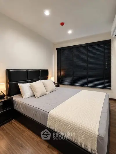Modern bedroom with sleek black blinds and cozy bedding in a stylish apartment.