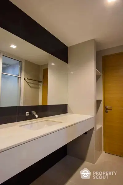 Modern bathroom with sleek design and large mirror, featuring a spacious countertop and elegant fixtures.