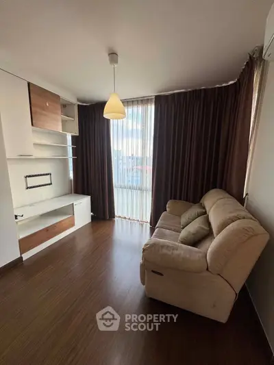 Cozy living room with plush sofa and modern entertainment unit, featuring floor-to-ceiling windows and elegant curtains.